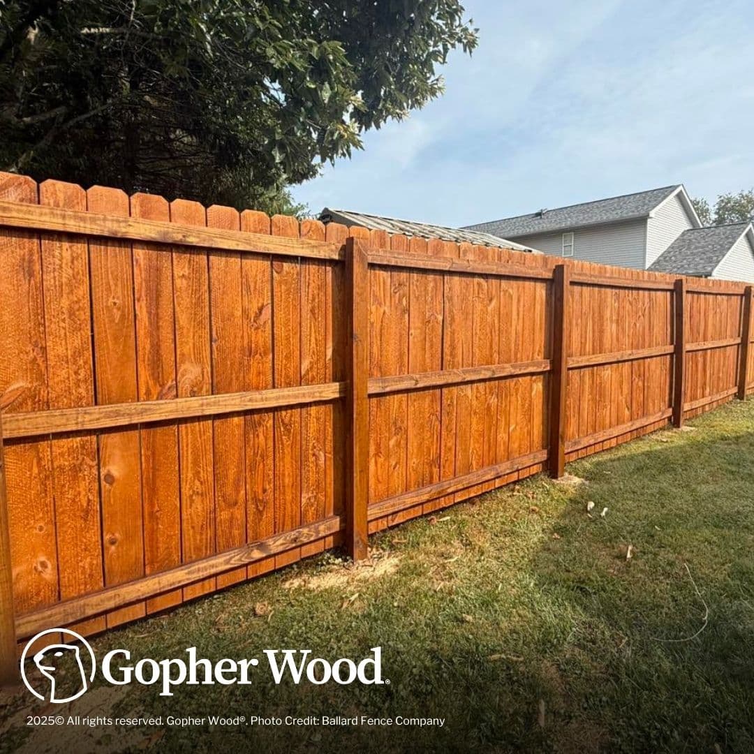 Richly stained wooden privacy fence with dog-ear pickets installed along a green grassy backyard.
